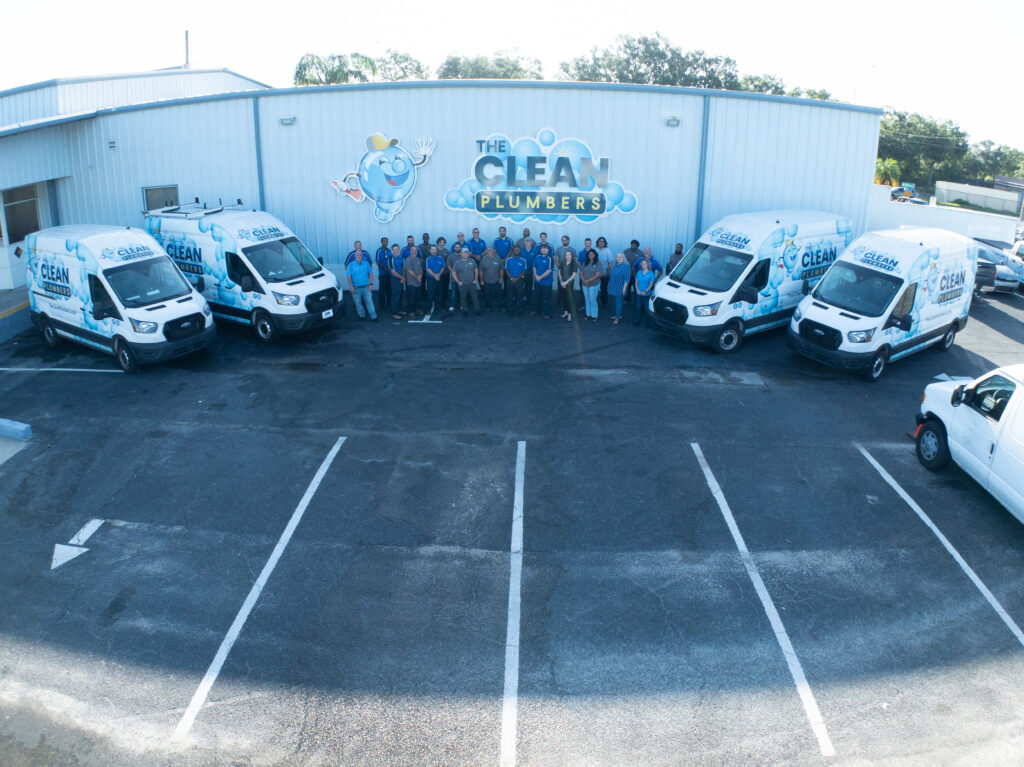 Multiple branded Clean Plumbers service vehicles lined up together in the company parking area.