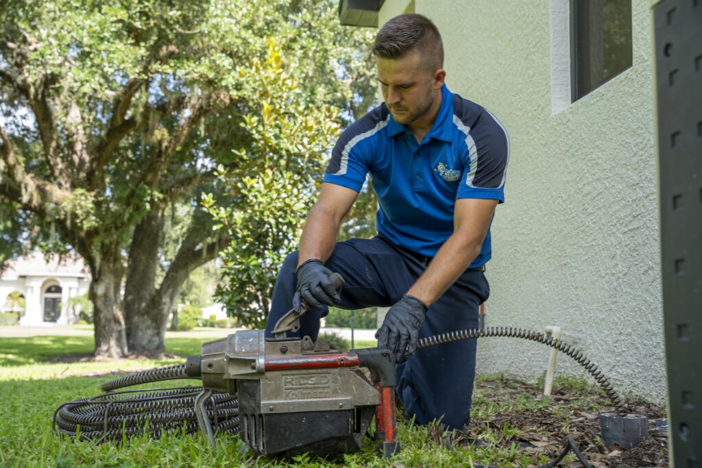 A Clean Plumbers technician operating professional drain-cleaning equipment outside a residence.