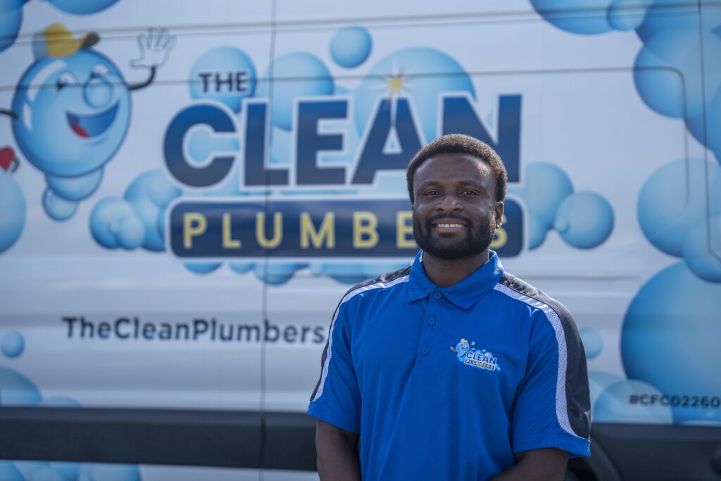 A Clean Plumbers service professional standing for a portrait in front of the company logo.