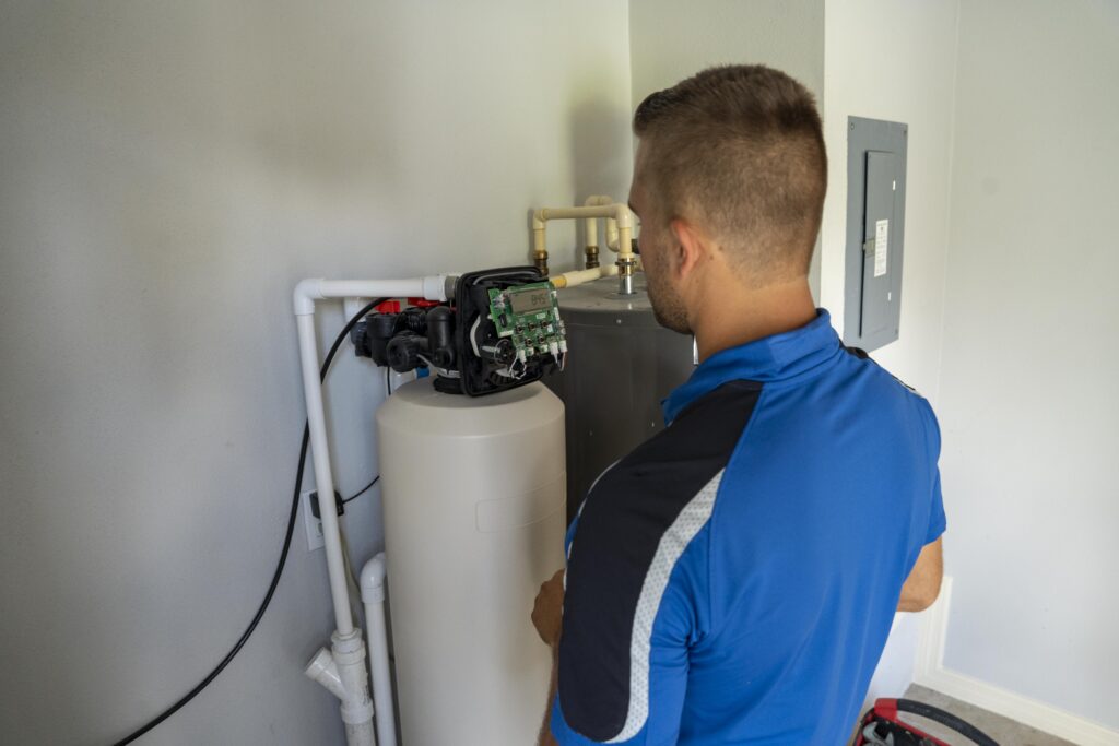 A Clean Plumbers technician servicing the control head of a residential water softener system.